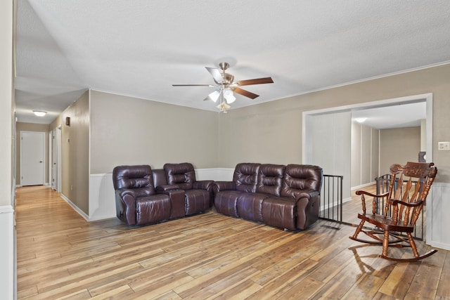 living room featuring ceiling fan, light hardwood / wood-style flooring, and a textured ceiling