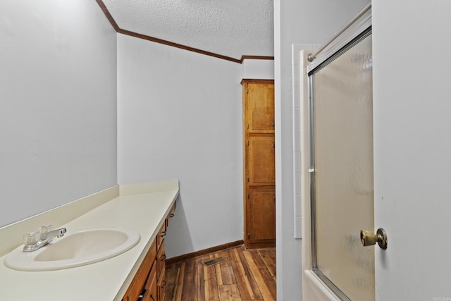 bathroom featuring hardwood / wood-style floors, a textured ceiling, combined bath / shower with glass door, vanity, and ornamental molding