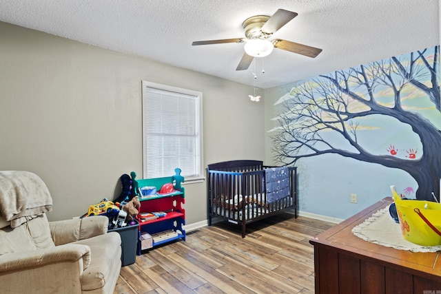 bedroom with a textured ceiling, light hardwood / wood-style flooring, a nursery area, and ceiling fan