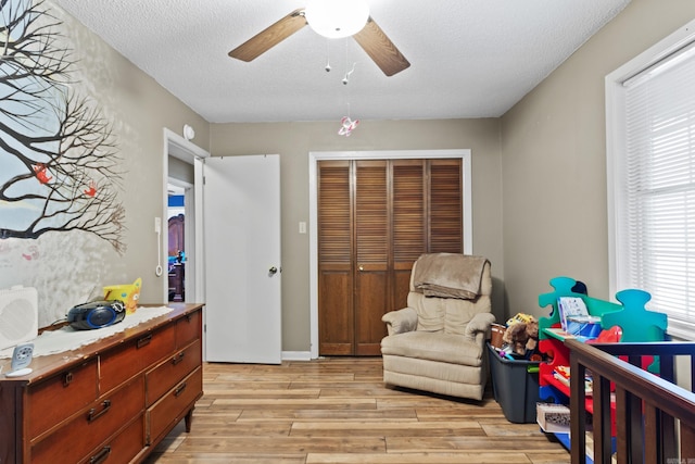 bedroom with ceiling fan, light hardwood / wood-style flooring, a textured ceiling, a closet, and a crib