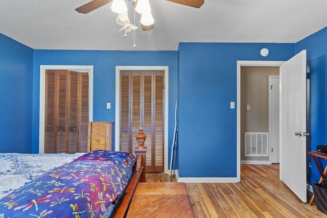 bedroom with ceiling fan, wood-type flooring, a textured ceiling, and two closets