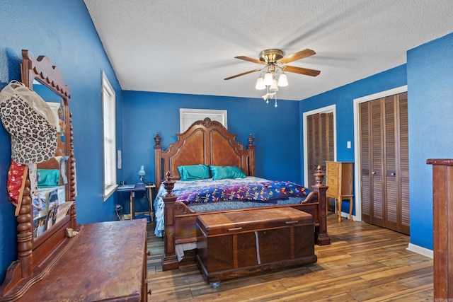 bedroom featuring hardwood / wood-style flooring, ceiling fan, a textured ceiling, and multiple closets