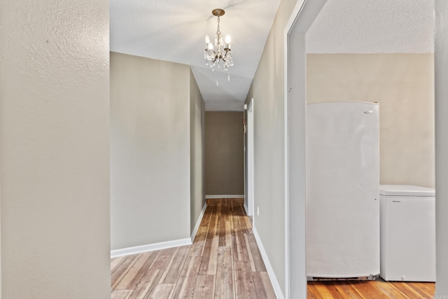 hallway featuring a chandelier, a textured ceiling, and light hardwood / wood-style floors