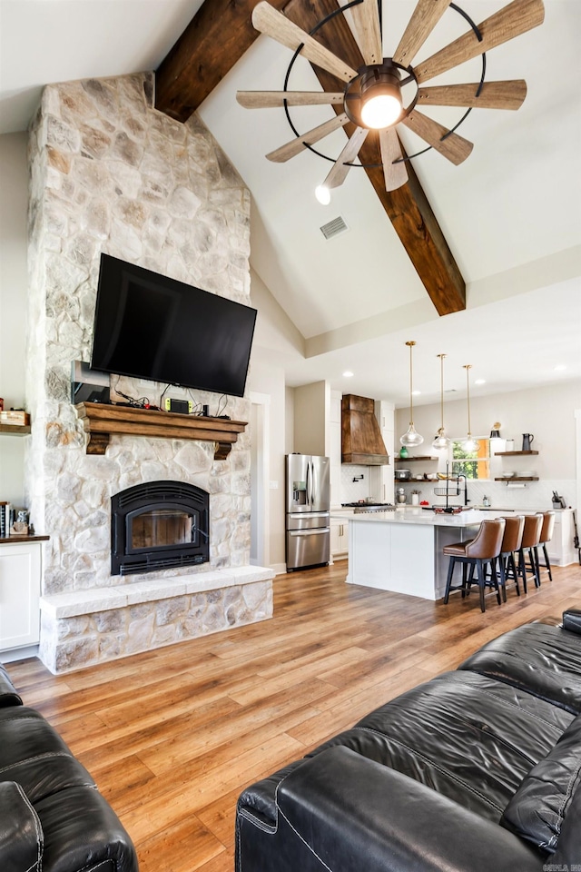 living room with ceiling fan, a stone fireplace, beamed ceiling, high vaulted ceiling, and light hardwood / wood-style floors