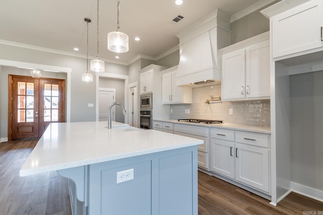 kitchen with white cabinets, hanging light fixtures, sink, an island with sink, and appliances with stainless steel finishes