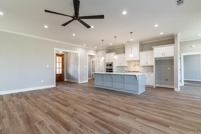 kitchen with white cabinetry, ceiling fan, decorative light fixtures, a kitchen island with sink, and custom range hood