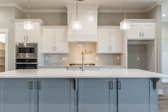 kitchen with appliances with stainless steel finishes, white cabinetry, hanging light fixtures, and a kitchen island with sink