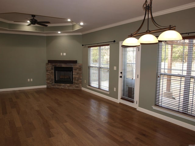 unfurnished living room with ceiling fan, a raised ceiling, a stone fireplace, dark hardwood / wood-style flooring, and ornamental molding