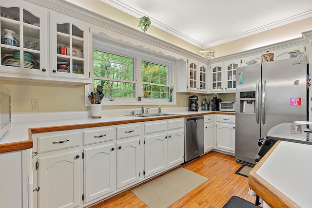 kitchen featuring white cabinets, crown molding, sink, appliances with stainless steel finishes, and light hardwood / wood-style floors