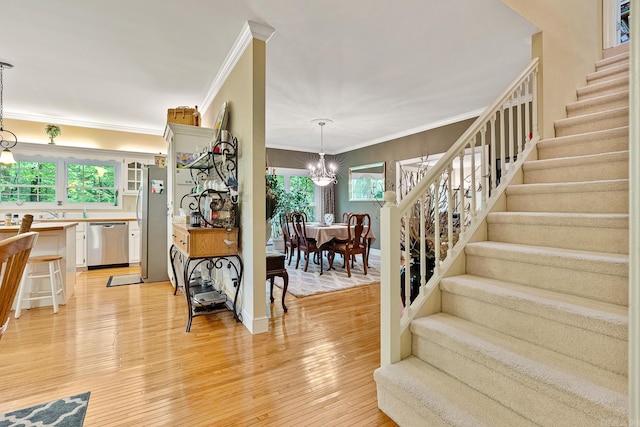 stairway with wood-type flooring, an inviting chandelier, and ornamental molding