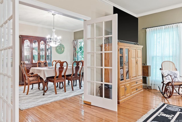 dining space featuring french doors, light wood-type flooring, ornamental molding, and a notable chandelier