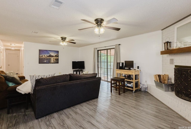 living room featuring ceiling fan, wood-type flooring, a textured ceiling, and a brick fireplace