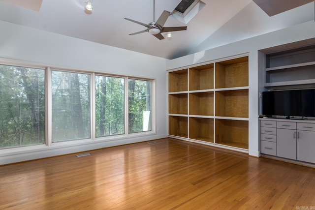 unfurnished living room with a wealth of natural light, lofted ceiling with skylight, built in features, and wood-type flooring