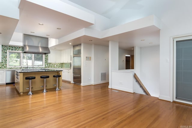 kitchen with backsplash, stainless steel appliances, wall chimney range hood, a center island, and white cabinetry