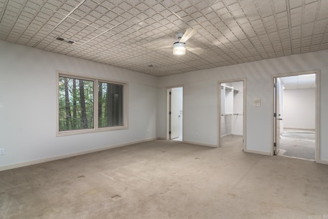 unfurnished bedroom with a walk in closet, ceiling fan, a closet, and light colored carpet