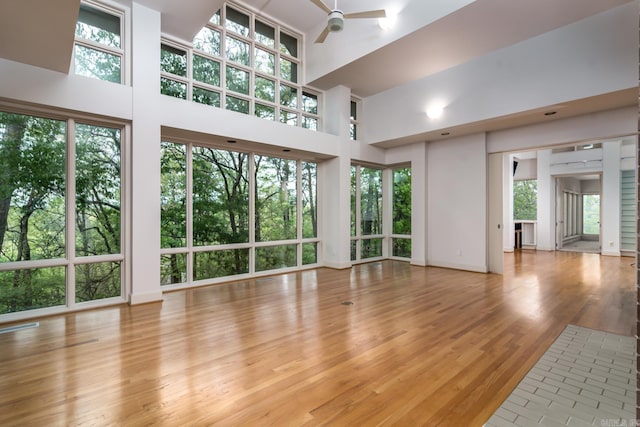 unfurnished living room featuring ceiling fan, a high ceiling, and light wood-type flooring