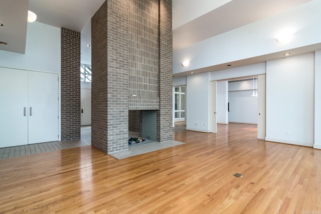 unfurnished living room with a fireplace, a high ceiling, and light wood-type flooring