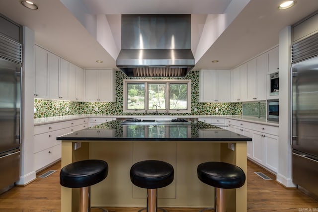 kitchen with built in appliances, white cabinetry, wall chimney exhaust hood, and a kitchen island