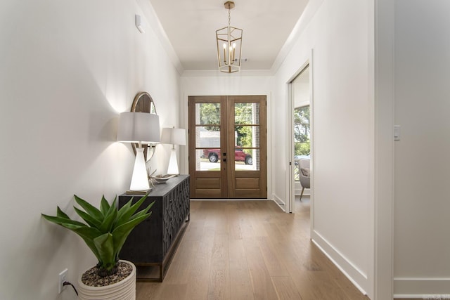 foyer entrance featuring a chandelier, crown molding, french doors, and light hardwood / wood-style floors