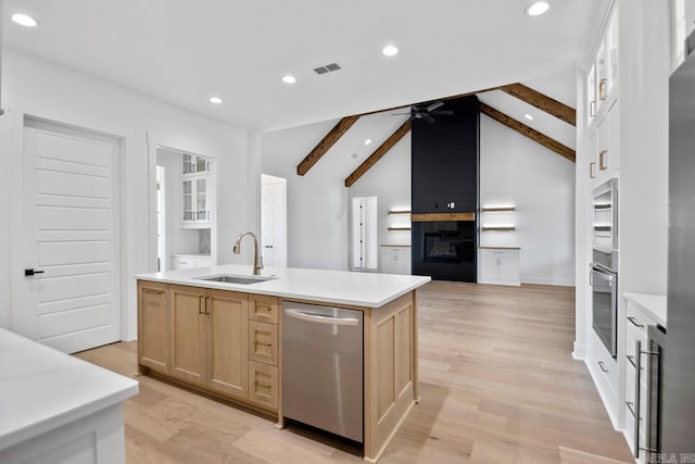 kitchen with a center island with sink, sink, vaulted ceiling with beams, light brown cabinetry, and stainless steel appliances