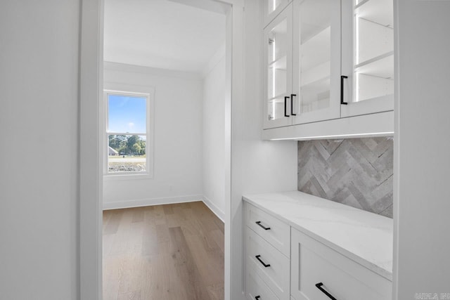 bar featuring backsplash, white cabinets, light hardwood / wood-style flooring, ornamental molding, and light stone countertops