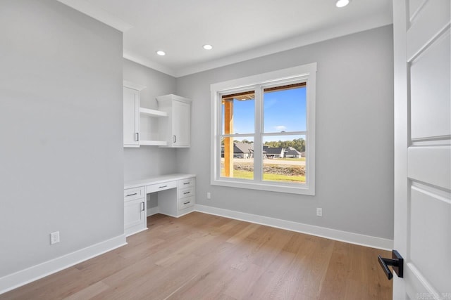 unfurnished office with crown molding, built in desk, and light wood-type flooring