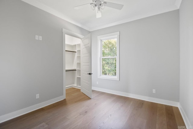 unfurnished bedroom featuring a walk in closet, ornamental molding, ceiling fan, wood-type flooring, and a closet