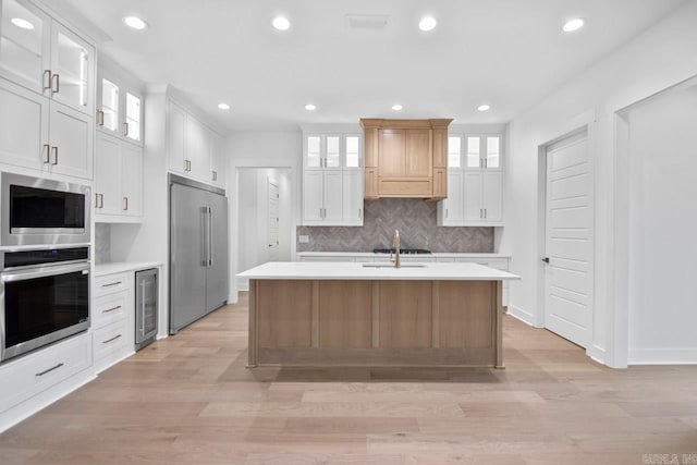 kitchen with built in appliances, light hardwood / wood-style floors, white cabinetry, and a kitchen island with sink