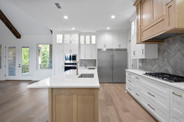 kitchen with built in appliances, white cabinets, sink, and an island with sink