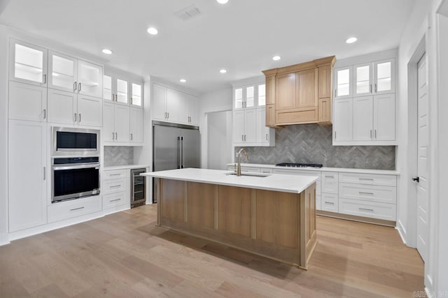 kitchen with a kitchen island with sink, white cabinetry, sink, and appliances with stainless steel finishes