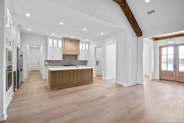 kitchen with light wood-type flooring, an island with sink, tasteful backsplash, white cabinetry, and stainless steel appliances