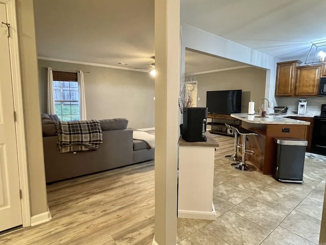 kitchen with black appliances, ceiling fan, crown molding, and a breakfast bar area