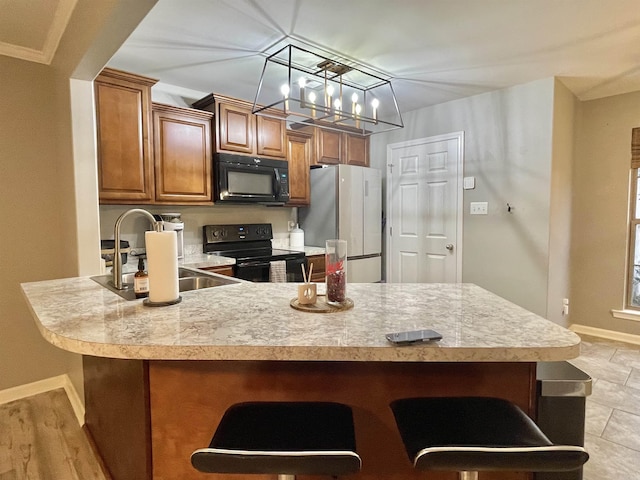 kitchen featuring a kitchen breakfast bar, ornamental molding, sink, black appliances, and hanging light fixtures