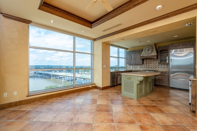 kitchen with a water view, a center island, appliances with stainless steel finishes, a tray ceiling, and custom range hood