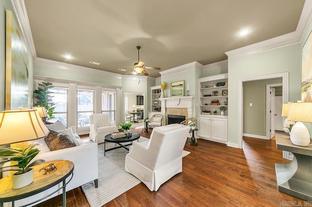 living room featuring ceiling fan, dark wood-type flooring, built in features, crown molding, and a fireplace