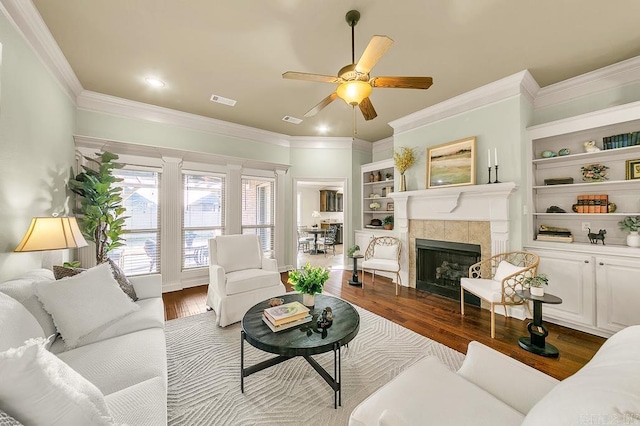 living room featuring a tile fireplace, built in shelves, dark hardwood / wood-style floors, and ceiling fan