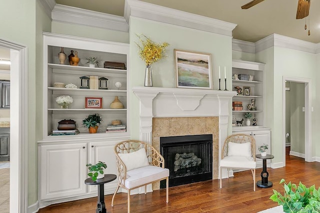 living area featuring built in shelves, ceiling fan, dark wood-type flooring, and a tiled fireplace