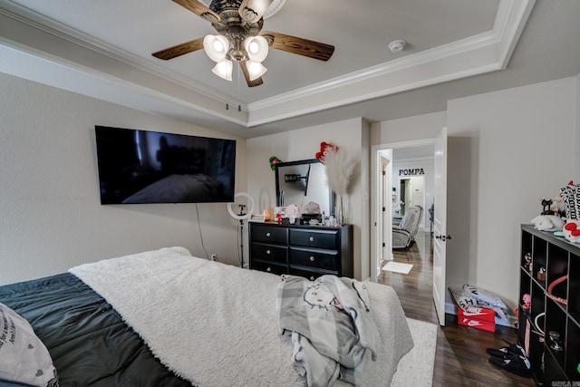 bedroom with ceiling fan, crown molding, a raised ceiling, and dark wood-type flooring