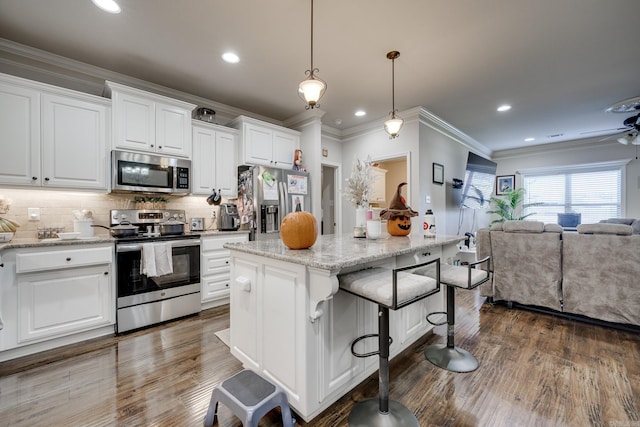 kitchen with stainless steel appliances, white cabinetry, decorative light fixtures, and a kitchen island