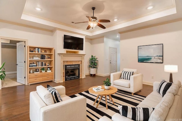 living room featuring ornamental molding, a tray ceiling, ceiling fan, dark hardwood / wood-style floors, and a tiled fireplace