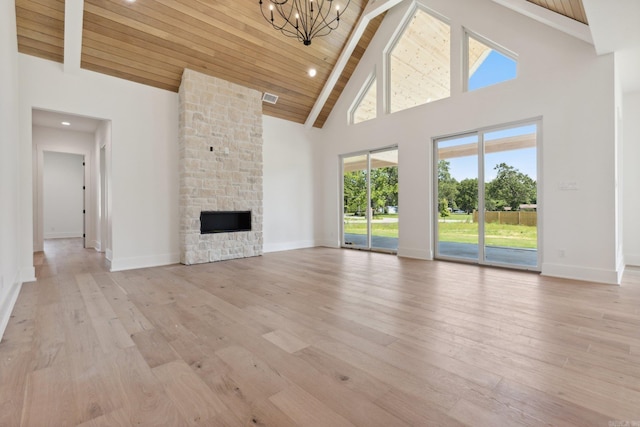 unfurnished living room featuring wooden ceiling, an inviting chandelier, a stone fireplace, a towering ceiling, and light hardwood / wood-style floors