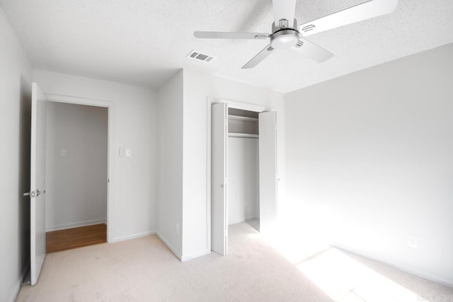 unfurnished bedroom featuring ceiling fan, light colored carpet, a textured ceiling, and a closet