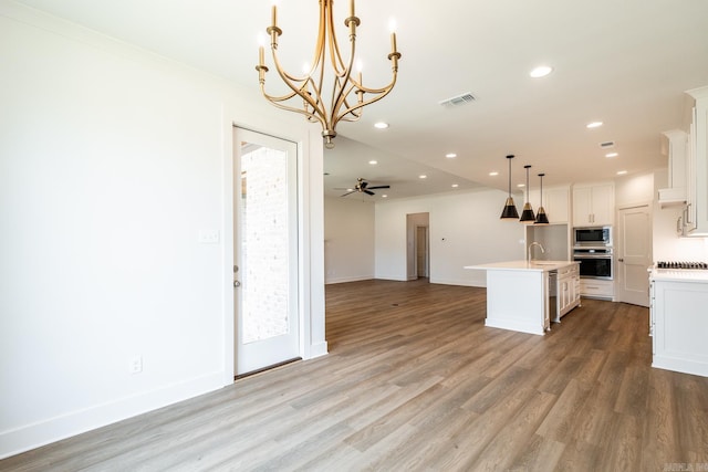 kitchen featuring ceiling fan with notable chandelier, stainless steel appliances, a kitchen island with sink, decorative light fixtures, and white cabinetry