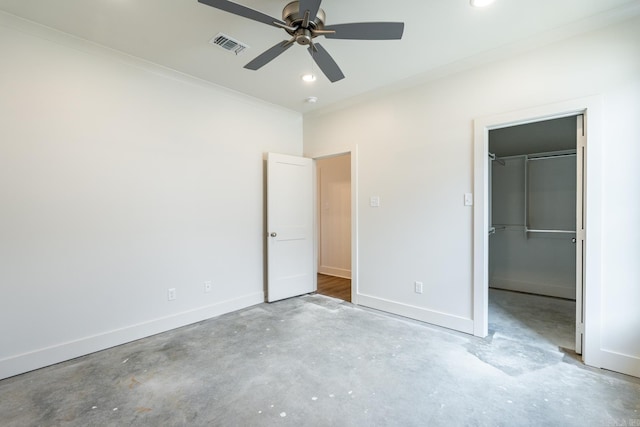 unfurnished bedroom featuring a walk in closet, ornamental molding, ceiling fan, concrete floors, and a closet