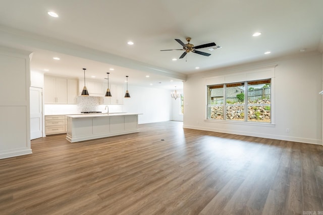 unfurnished living room featuring hardwood / wood-style flooring, ceiling fan with notable chandelier, and sink