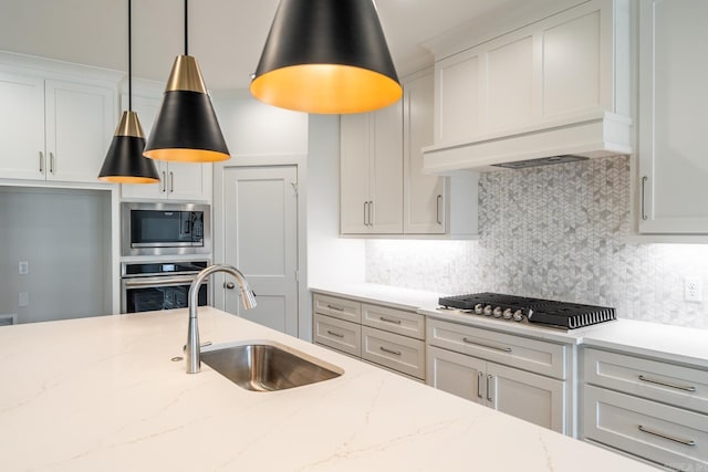 kitchen with sink, light stone counters, decorative light fixtures, white cabinets, and appliances with stainless steel finishes