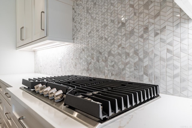 room details featuring white cabinets, backsplash, light stone counters, and stainless steel gas cooktop