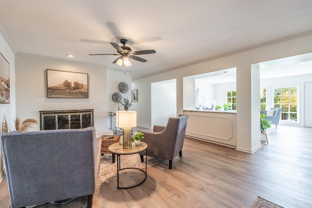 living area featuring light hardwood / wood-style floors, a brick fireplace, ceiling fan, and crown molding