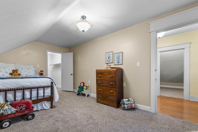 bedroom with a walk in closet, a closet, carpet, and vaulted ceiling