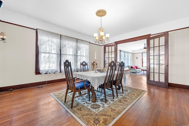 dining area featuring ceiling fan with notable chandelier, wood-type flooring, and french doors